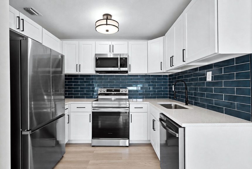After: remodeled kitchen with white shaker cabinets, quartz counters, blue glass backsplash and stainless appliances