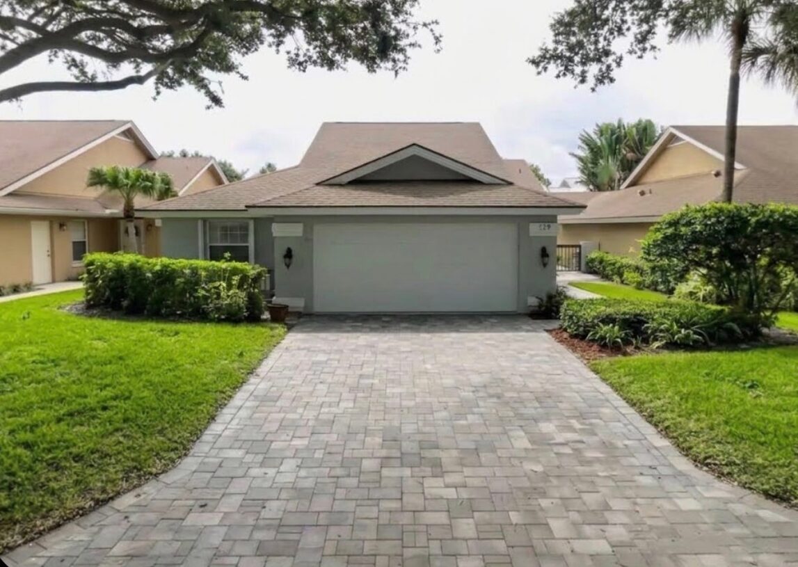 Before: Jupiter home in The Bluffs with a gray exterior with a two-car garage, dated trim and a paver driveway
