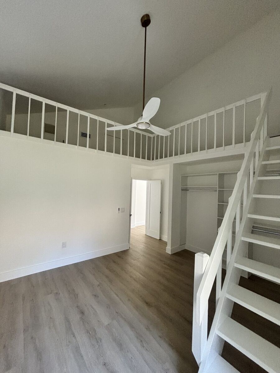 Vaulted living space with white railing loft stairs and a new ceiling fan