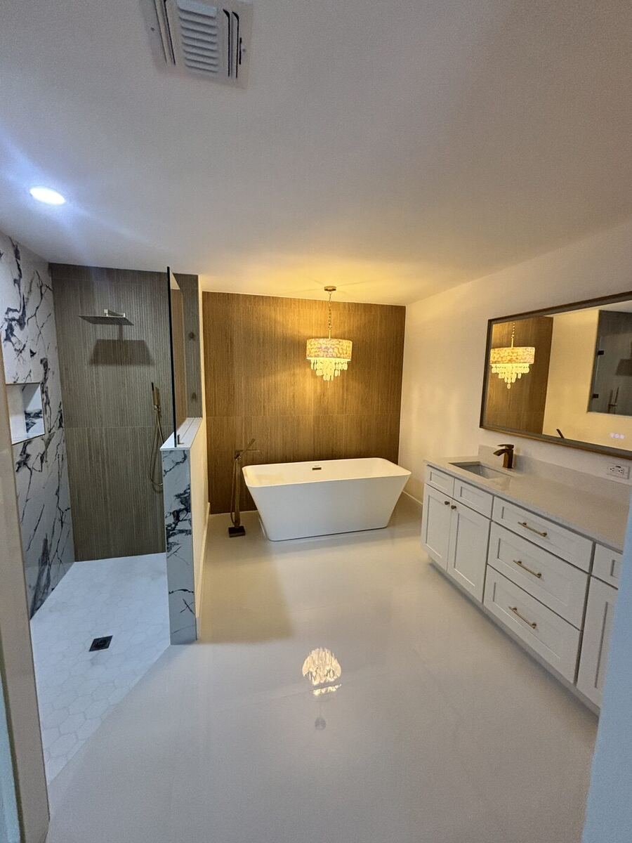 Primary bath with freestanding tub, wood accent wall, chandelier and white tile floor