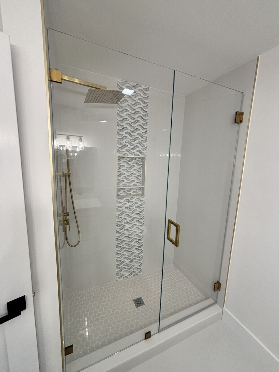 Frameless glass shower with a mosaic tile niche and gold fixtures