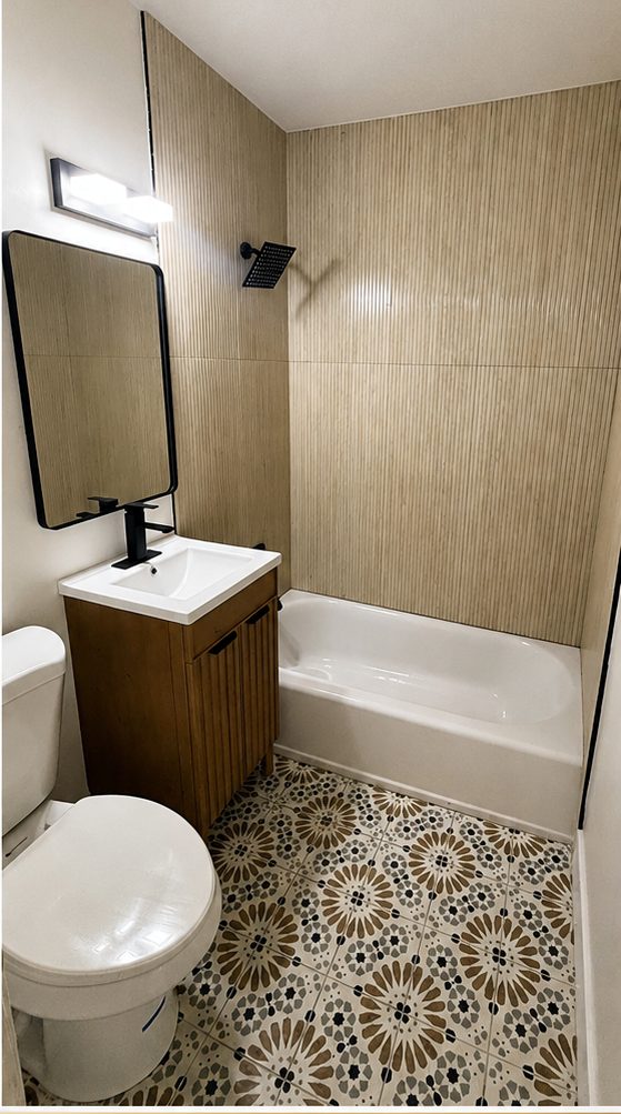After: remodeled bathroom with a fluted tile tub surround, wood vanity, black fixtures and patterned tile floor