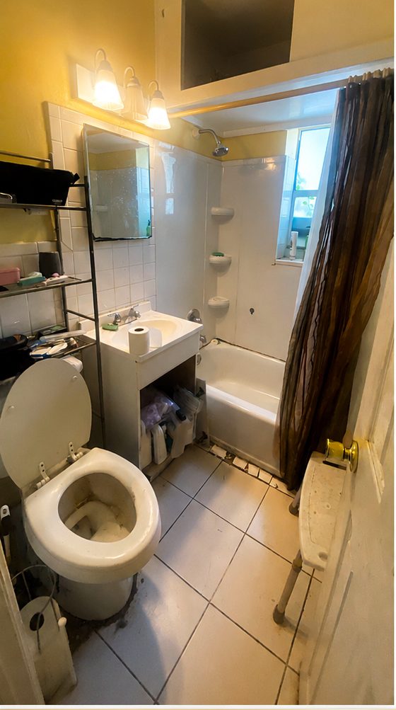 Before: dated bathroom with a worn tub surround, small vanity and cracked tile floor